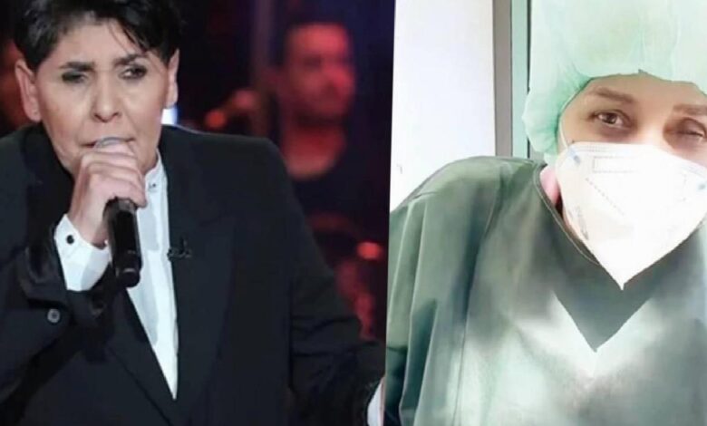 Man in a black suit sings into a microphone on a dim stage; right side shows a masked healthcare worker in green scrubs and a cap.