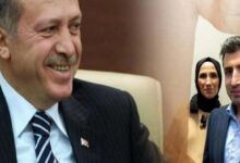 Two men in suits smiling in the foreground, with a woman wearing a headscarf in the background.