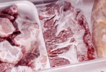 Frozen raw beef cuts in white Styrofoam trays, heavily frosted and stored in a freezer.