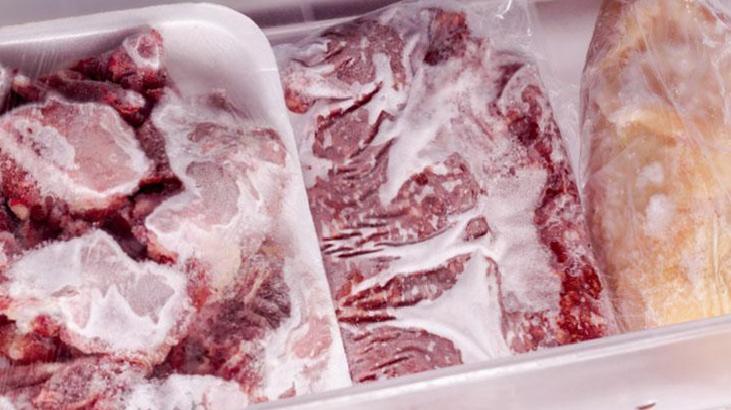 Frozen raw beef cuts in white Styrofoam trays, heavily frosted and stored in a freezer.