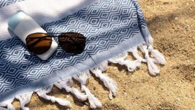 Sunglasses and a sunscreen bottle rest on a blue geometric towel spread on sandy beach.