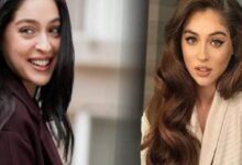 Two women posing indoors: one with long dark hair smiling, the other with long wavy brown hair wearing a beige blazer.