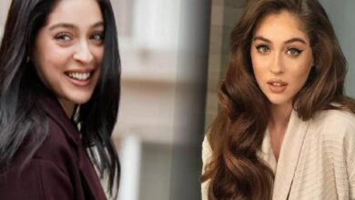 Two women posing indoors: one with long dark hair smiling, the other with long wavy brown hair wearing a beige blazer.