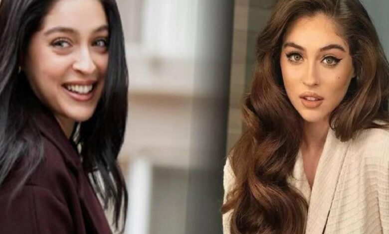 Two women posing indoors: one with long dark hair smiling, the other with long wavy brown hair wearing a beige blazer.