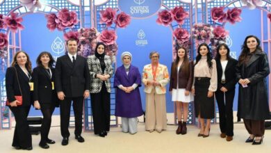 Twelve people posing for a photo in front of a blue floral backdrop with 'Cemre Çarşısı' logos.
