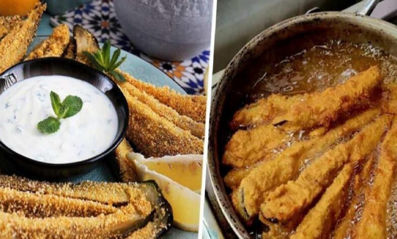 Crispy breaded zucchini sticks with a creamy herb dip in a black bowl and lemon wedges on a decorative plate.