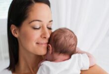 Mother cradling a newborn baby close to her shoulder, both eyes closed in a tender, peaceful moment.