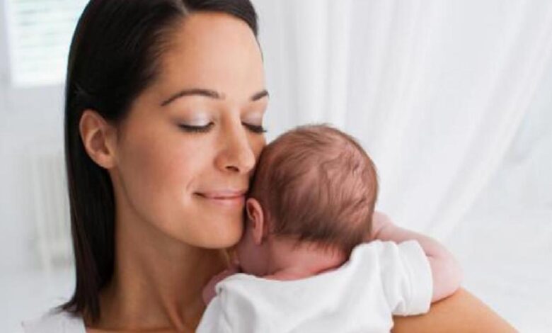 Mother cradling a newborn baby close to her shoulder, both eyes closed in a tender, peaceful moment.