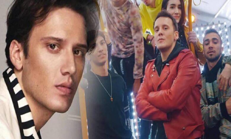 Close-up of a young man in the foreground with a striped scarf, others posing behind in a brightly lit hallway or studio.