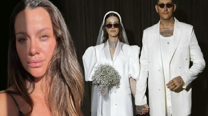 Close-up of a woman with long brown hair; in the background, a bride in a white gown with a bouquet and a man in a white suit standing together.