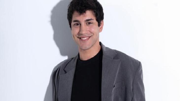 Smiling man in a gray blazer and black shirt posing against a white background.