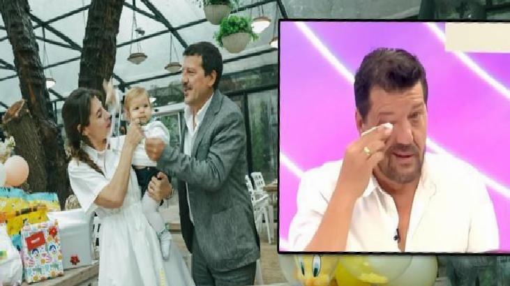 Mother and father with their baby at a celebration, under a bright indoor setting; an inset TV screen shows a man wiping his eye.