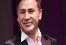 Smiling man in a white shirt and glittering jacket on stage performing for an audience.