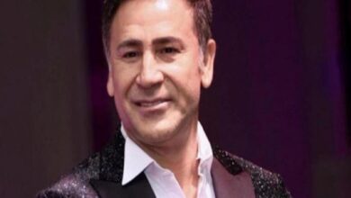 Smiling man in a white shirt and glittering jacket on stage performing for an audience.