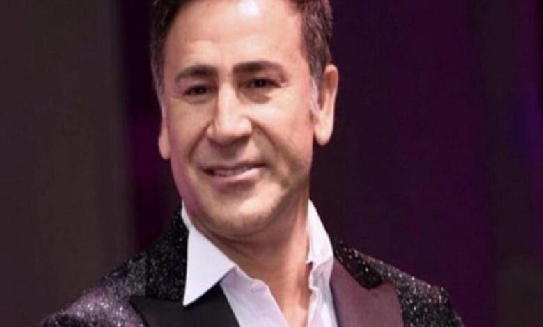 Smiling man in a white shirt and glittering jacket on stage performing for an audience.