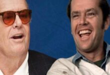 Two men laughing together against a blue backdrop; one wears sunglasses and a suit, the other in a light jacket.