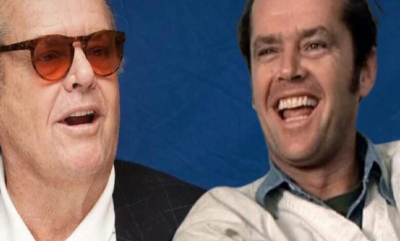 Two men laughing together against a blue backdrop; one wears sunglasses and a suit, the other in a light jacket.