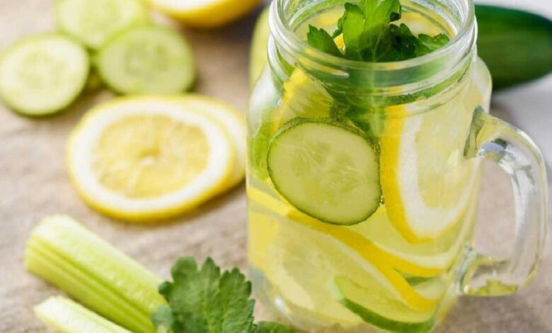 Glass mason jar of lemonade with cucumber, lemon slices and mint leaves, on a wooden table with celery in the foreground