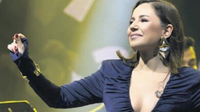 Female singer on stage with one arm raised, wearing a navy dress and large earrings, performing under bright stage lights.