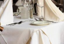 Formal dining table set with white tablecloth, folded napkins, plates, cutlery, and wine glasses ready for guests.