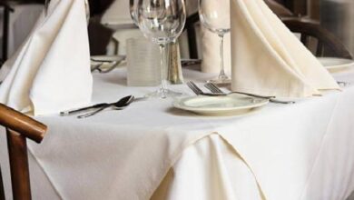 Formal dining table set with white tablecloth, folded napkins, plates, cutlery, and wine glasses ready for guests.