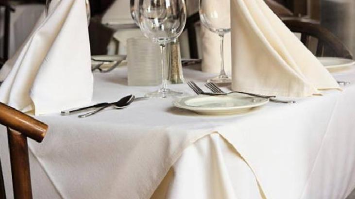 Formal dining table set with white tablecloth, folded napkins, plates, cutlery, and wine glasses ready for guests.
