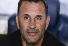 Close-up portrait of a middle-aged man with short dark hair and stubble, looking at the camera with a neutral expression.
