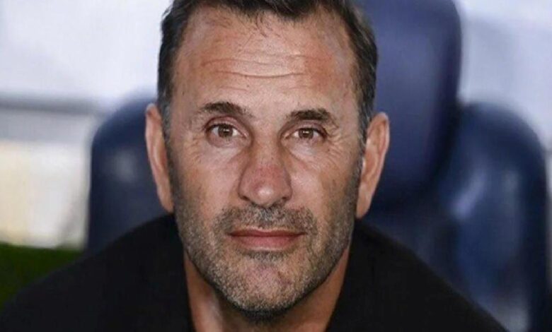 Close-up portrait of a middle-aged man with short dark hair and stubble, looking at the camera with a neutral expression.