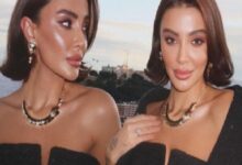 Two women in black off-shoulder outfits posing on a rooftop by the ocean, wearing statement necklaces and bold makeup as the sun sets behind them.