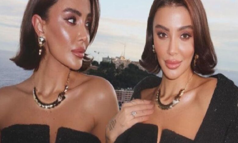 Two women in black off-shoulder outfits posing on a rooftop by the ocean, wearing statement necklaces and bold makeup as the sun sets behind them.