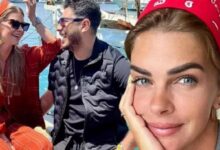 Woman in a red bandana faces the camera, resting her cheek on her hand, with two friends chatting and smiling on a sunny boat in the background.