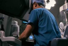 Surgeon in blue scrubs operating at a robotic surgical system in a high-tech operating room.