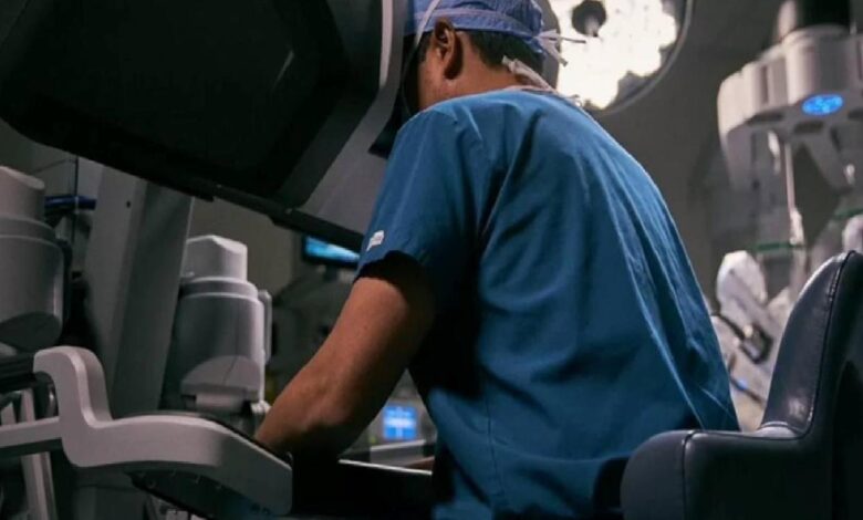 Surgeon in blue scrubs operating at a robotic surgical system in a high-tech operating room.