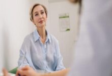 Professional woman in a light blue striped shirt seated at a desk, listening during a discussion in an office setting.