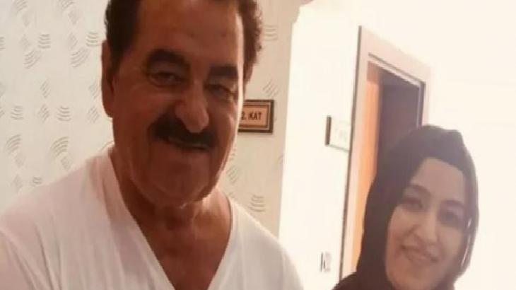 Two people pose indoors: a smiling man with a mustache in a white shirt and a woman in a dark hijab.