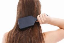 Person brushing their long brown hair with a large dark paddle brush against the back of their head reflects grooming.