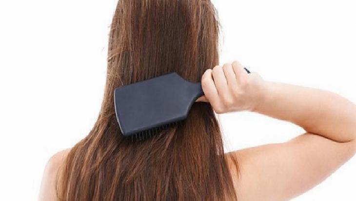 Person brushing their long brown hair with a large dark paddle brush against the back of their head reflects grooming.