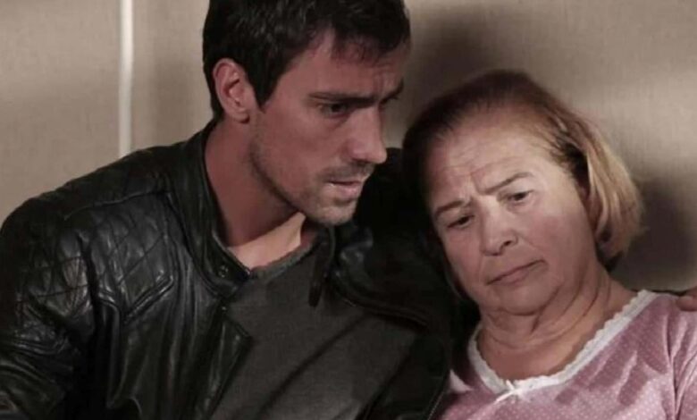 A young man in a black leather jacket comforts an older woman, both looking somber.