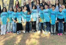 Group of children in turquoise TEGV shirts posing for a photo with adults outdoors in a park.