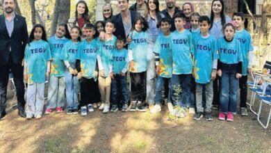 Group of children in turquoise TEGV shirts posing for a photo with adults outdoors in a park.