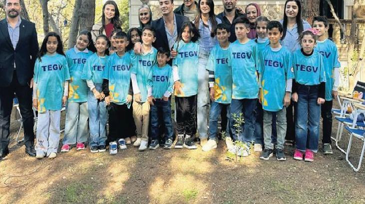 Group of children in turquoise TEGV shirts posing for a photo with adults outdoors in a park.