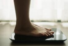 Bare feet standing on a glass digital scale in a bright room, ready to weigh herself/himself.