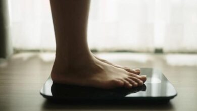 Bare feet standing on a glass digital scale in a bright room, ready to weigh herself/himself.