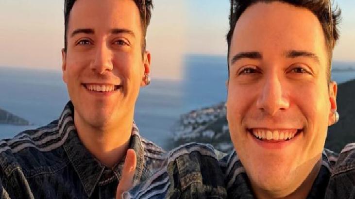 Two men smiling for a selfie on a coastal overlook at sunset, with the sea and cliffs in the background, wearing denim jackets.