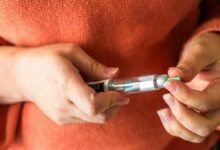 Person in an orange sweater preparing a syringe, drawing fluid into the barrel from a vial