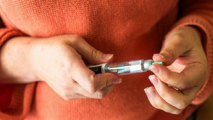 Person in an orange sweater preparing a syringe, drawing fluid into the barrel from a vial