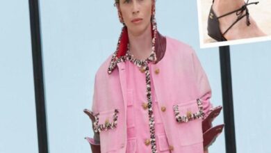 Model wearing a pink jacket with black-and-white braided trim and gold buttons; inset shows a black strappy sandal.