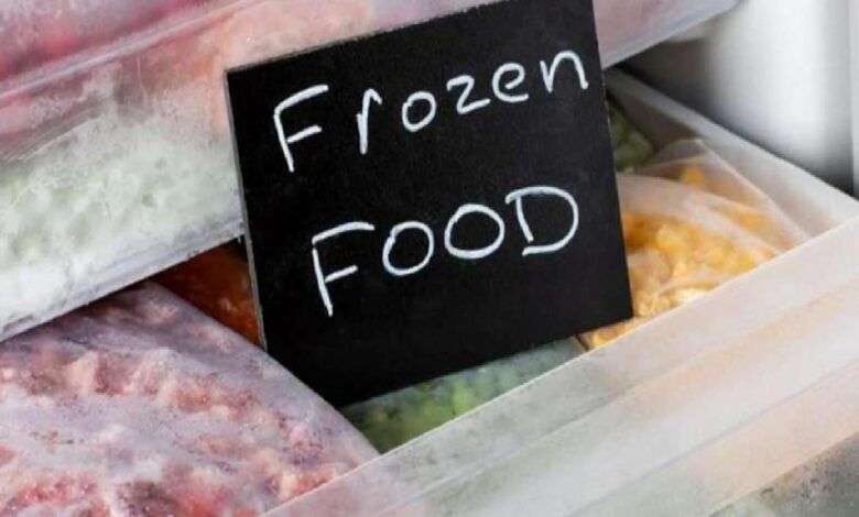 Black chalkboard sign reading 'Frozen Food' inside a freezer with bags of frozen items surrounding it.