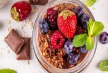 Jar of chocolate granola topped with strawberries, blueberries, raspberries, and mint leaves; fresh fruit dessert or breakfast parfait.