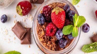 Jar of chocolate granola topped with strawberries, blueberries, raspberries, and mint leaves; fresh fruit dessert or breakfast parfait.